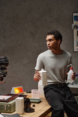 Genç Afrikalı Amerikalı adam iyi organize edilmiş bir karanlık odada fotoğraf filmi kimyasallarını dikkatlice ölçüyor.
