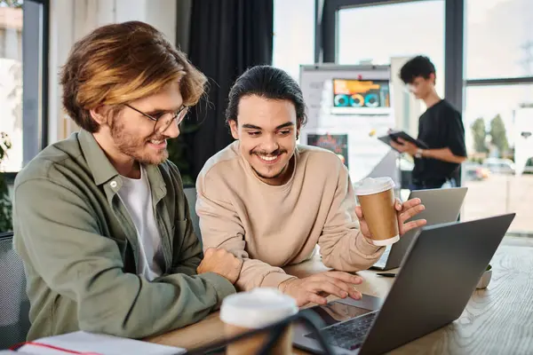 stock image joyful startup team members discussing project and working on laptops in coworking space, men in 20s