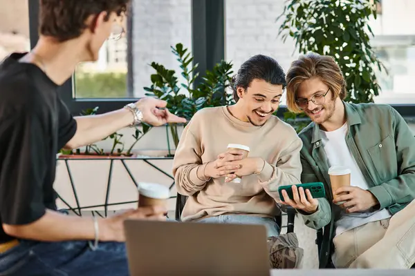 Ofiste kahve molası sırasında sohbet eden ve akıllı telefondan video izleyen neşeli genç adamlar.