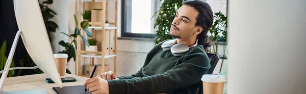 stock image Young man doing post-production work, focused on retouching on a tablet near monitor, banner