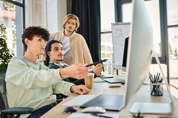 stock image post production team discussing retouching project on monitor in a well-lit office, men in 20s