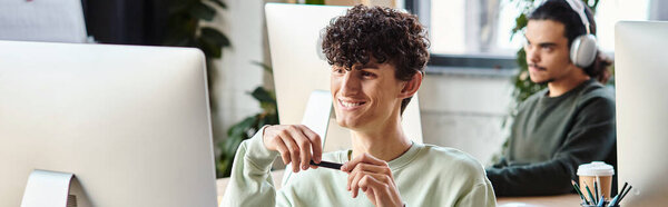 satisfied curly man engaged in retouching work, holding stylus pen and looking at monitor, banner
