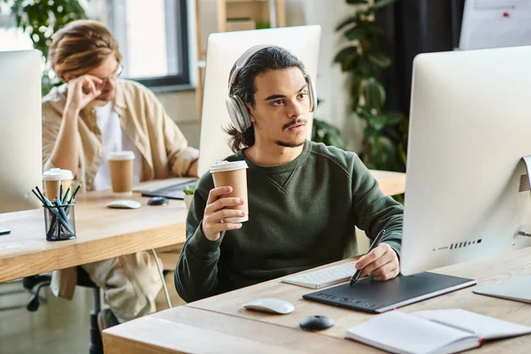 在办公室里手持咖啡和使用图形平板电脑的耳机的沉思的男性专业人员 — 图库照片