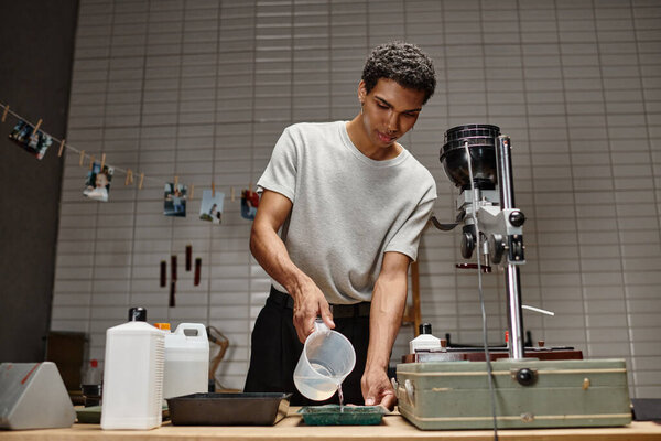 тщательный процесс разработки пленки, африканский американец наливает химический раствор в поднос