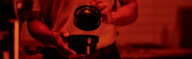 Kesilmiş fotoğrafçı pankartı elinde film kutusu ve kırmızı karanlık odada fotoğraf tab ediyor.
