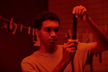 african american photographer examines developed film strip, bathed in darkroom with red light clipart