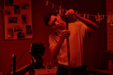 Odaklanmış Afrikalı Amerikalı fotoğrafçı film şeridi geliştirdi, kırmızı karanlık odada yıkandı.