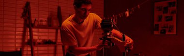 Fotoğrafçı, karanlık odada kırmızı ışık ve pankartıyla filmi büyütme sürecine odaklanıyor.
