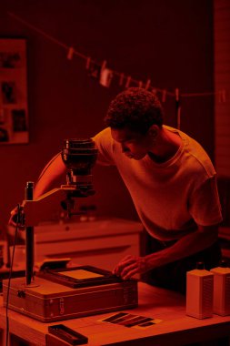 Afrikalı Amerikalı fotoğrafçı, bir karanlık odanın kırmızı ışığı altında fotoğrafı inceliyor.