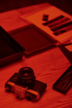 Analog kamera ve kırmızı ışık altında film geliştirmek için araçları olan bir karanlık oda masası.