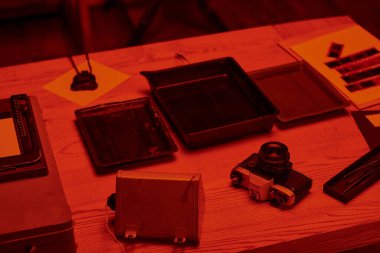 Analog kamera ve film geliştirme araçlarıyla dolu bir masa. Karanlık odada kırmızı ışık ve nostalji ile.