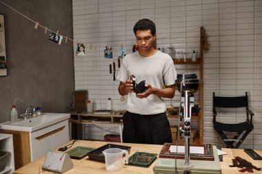 Siyah fotoğrafçı, analog ekipmanlarla çevrili modern bir karanlık odada film geliştiricisini inceliyor.