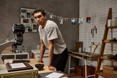 Analog ekipmanlarla çevrili Afrikalı Amerikalı fotoğrafçı modern karanlık odada duruyor.