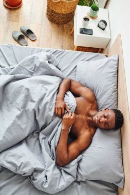 Genç ve kaslı Afro-Amerikan erkeği sabahları rahat bir yatakta uyuyor.