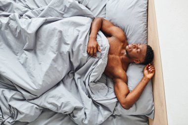 top view of handsome athletic african american man sleeping on comfortable bed at home in morning clipart