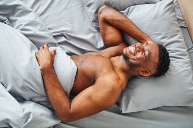 top view of happy muscular african american man dreaming and smiling on grey comfortable bedding clipart