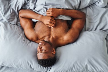 Güçlü vücutlu Afro-Amerikan adam, evinde rahat bir yatak hayal ediyor.