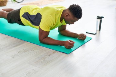 Sportif Afro-Amerikalı adam spor şampanyası ve akıllı telefonun yanında tahta poz veriyor.