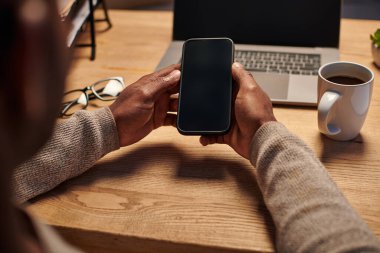 neşeli Afrikalı Amerikalı adam akıllı telefonla konuşuyor ve evde çalışırken not defterine yazıyor.