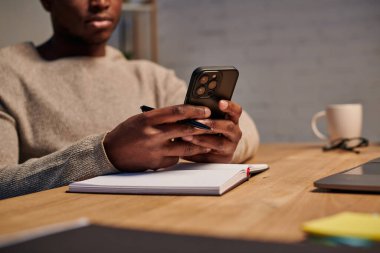 Afro-Amerikan Serbest Çalışan 'ın merkez ofisteki defterin yanında akıllı telefondan sohbet edişini izledik.