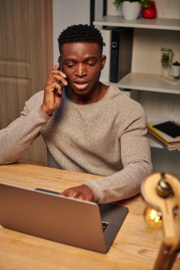 Genç odaklı Afrikalı Amerikalı serbest çalışan ve bilgisayarın yanında akıllı telefondan konuşan.