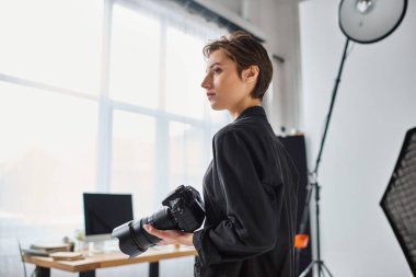 attractive young female photographer in everyday clothes posing in her studio and looking away clipart