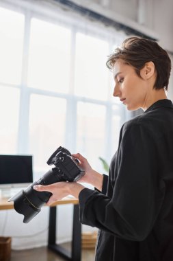 Günlük kıyafetli genç ve güzel bir kadın fotoğrafçı stüdyosundaki fotoğraf makinesine bakıyor.