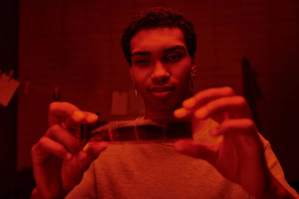 stock image satisfied african american photographer examine developed film strip in a red-lit darkroom