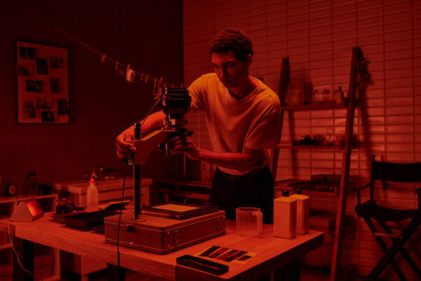 In a darkroom with red light, photographer focuses intently on delicate process of enlarging film