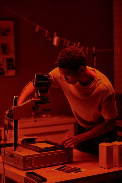 african american photographer inspecting photo negative under the red safety light of a darkroom