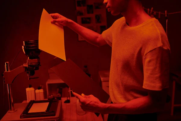 stock image african american photographer ensures quality of photo print while holding envelope in darkroom