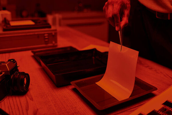 cropped shot of photographer delicately immerses photo paper in a darkroom bath with chemicals