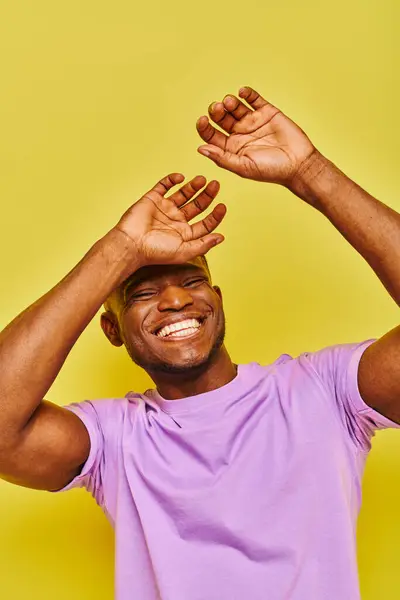 stock image overjoyed and stylish african american man in purple t-shirt gesturing laughing on yellow backdrop