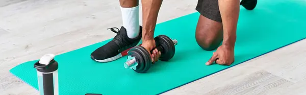 stock image cropped view of african american guy training with dumbbell on fitness mat at home, banner