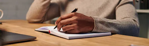 cropped view of african american freelancer writing in notebook while working at home, banner