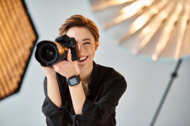 Kısa saçlı, neşeli, güzel bir kadın stüdyosunda poz veriyor ve fotoğraf çekiyor.