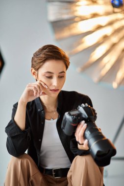 Genç ve güzel bir bayan fotoğrafçı günlük kıyafetlerle stüdyodaki fotoğraf makinesine bakıyor.