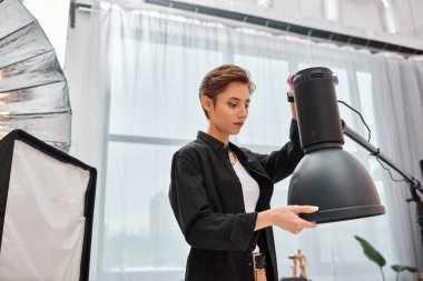 beautiful young brunette woman with short hair looking at her photography equipment in her studio clipart