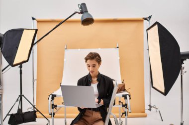 Çekici kısa saçlı fotoğrafçı stüdyosunda oturmuş bilgisayarını kullanarak fotoğrafları rötuşluyor.