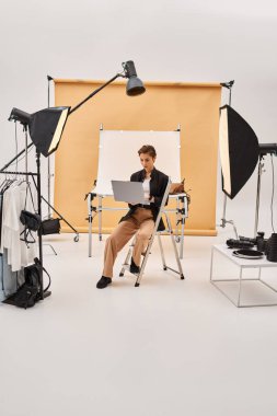 Güzel, kısa saçlı fotoğrafçı stüdyosunda oturmuş bilgisayarını kullanarak fotoğrafları rötuşluyor.