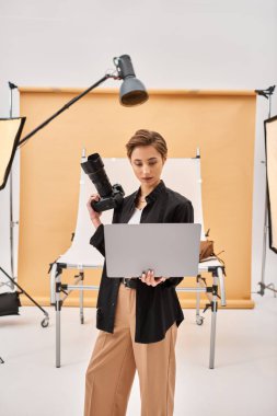 Güzel görünümlü, sıradan giyinmiş, fotoğraf makinesini ve laptopunu kullanan genç bir kadın.