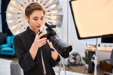 Modern fotoğraf makinesiyle stüdyosunda fotoğraf çeken günlük kıyafetli, çekici bir kadın.