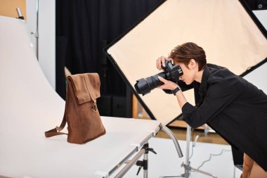 Harika kısa saçlı kadın fotoğrafçı stüdyosunda kahverengi derili sırt çantasının fotoğraflarını çekiyor.