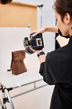 Çekici kısa saçlı kadın fotoğrafçı stüdyosunda kahverengi derili sırt çantasının fotoğraflarını çekiyor.