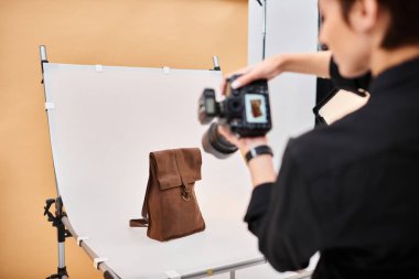Güzel kısa saçlı kadın fotoğrafçı stüdyosunda kahverengi derili sırt çantasının fotoğraflarını çekiyor.