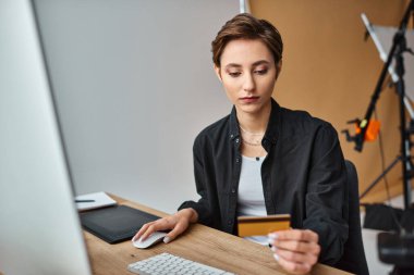 Rahat giyinen çekici genç bayan fotoğrafçı kredi kartıyla internetten ödeme yapıyor.