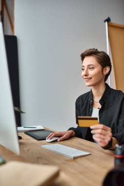 Mutlu çekici kadın fotoğrafçı internetten kredi kartını kullanıyor ve mutlu bir şekilde gülümsüyor.