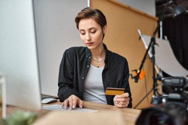 Rahat giyinen çekici genç bayan fotoğrafçı kredi kartıyla internetten ödeme yapıyor.