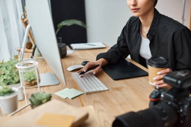 Kahve tutan, bilgisayarla çalışan ve tablet çizen genç bayan tasarımcı görüntüsü.
