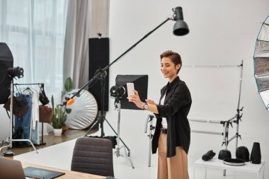 joyful young female photographer with short hair making stories for her social media in her studio clipart